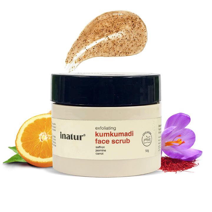 Jar of inatur Kumkumadi face scrub with a scoop of scrub above it, surrounded by an orange, saffron flower, and strands on a white background.